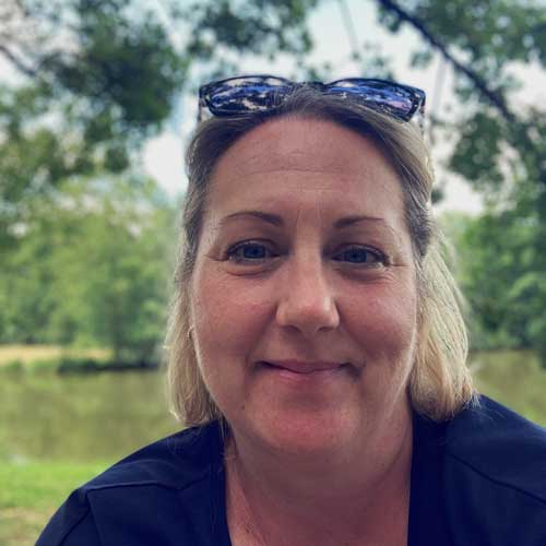 Mme Knight sitting outside on a summery day with sunglasses on head and green fields in the background